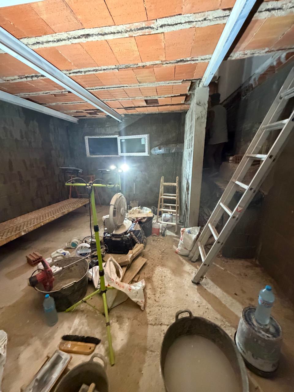 Sótano con paredes levantadas, ventana colocada al fondo y herramientas de obra en el suelo