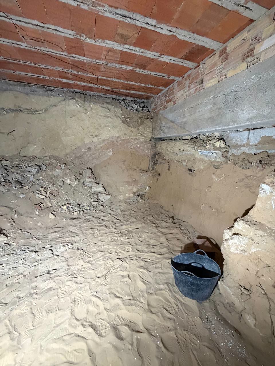 Espacio bajo el forjado de ladrillo, con tierra excavada en el suelo y un capazo negro en una esquina