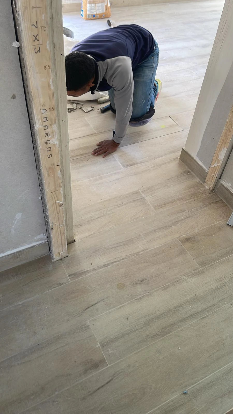 Operario arrodillado trabajando sobre un pavimento de aspecto madera.