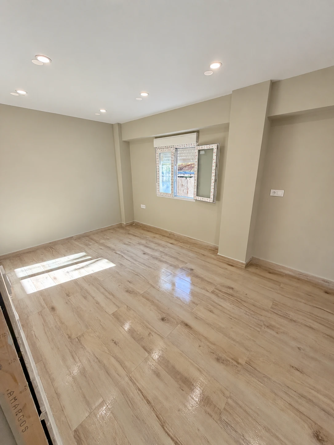 Estancia con suelo de aspecto madera, ventana y focos empotrados.