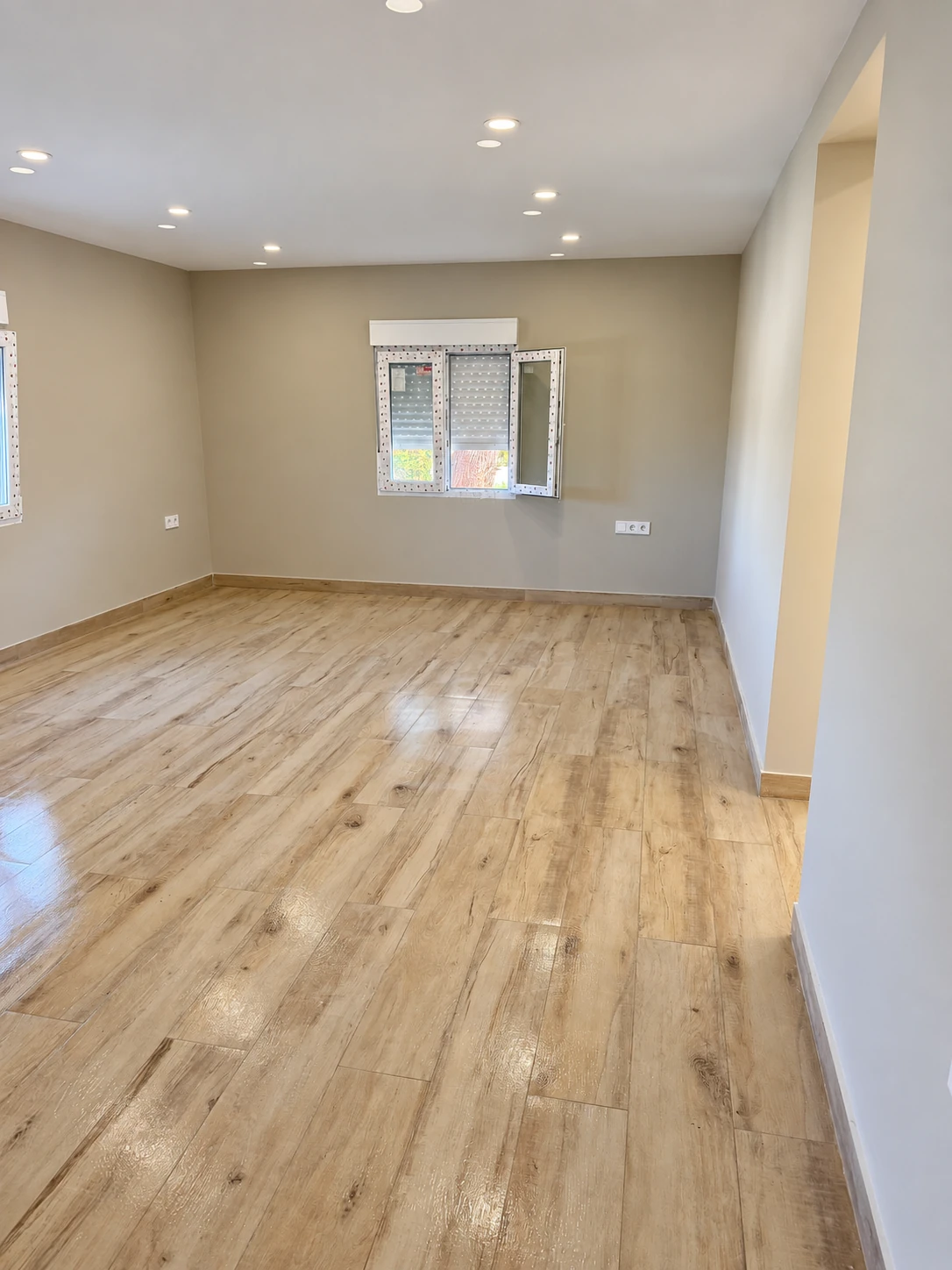 Interior sin amueblar con pavimento de aspecto madera y focos en el techo.