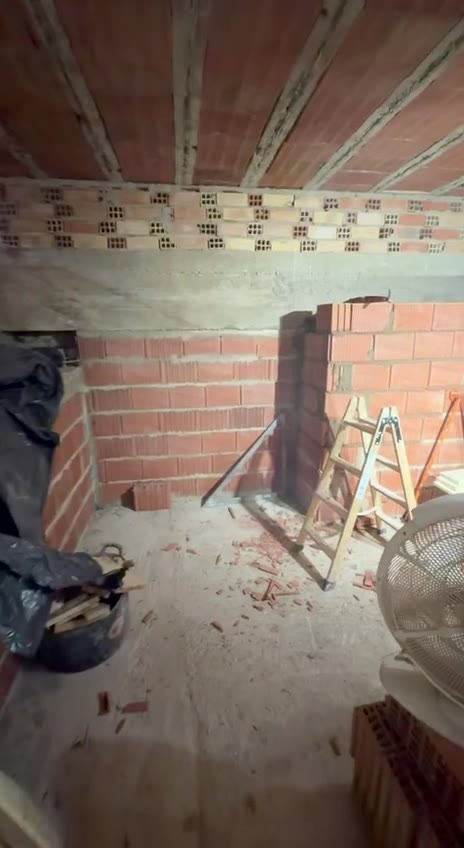 Muros de ladrillo en construcción sobre la base ya hecha, con una escalera de tijera al lado